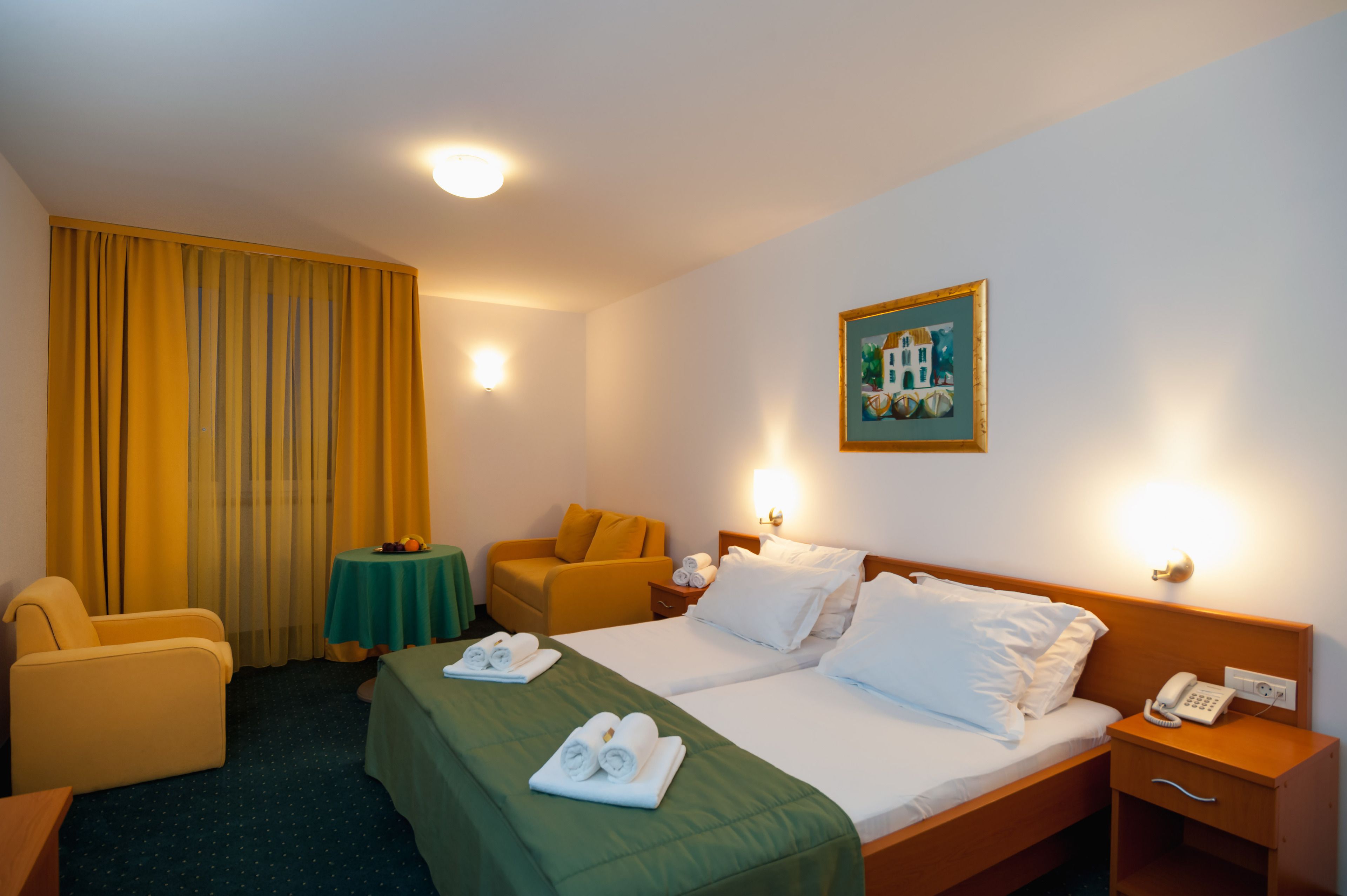 Ein Hotelzimmer mit zwei Betten, einem Schreibtisch, einem Stuhl, einem Tisch mit Obst und einem Bild an der Wand.