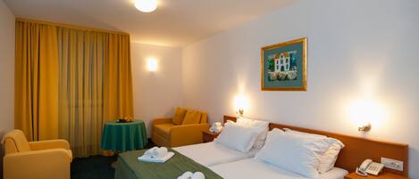 Une chambre d’hôtel avec deux lits, un bureau, une chaise, une table avec des fruits et un tableau au mur.
