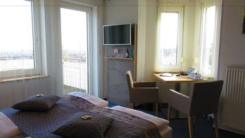 A hotel room with a bed, a desk, a chair, a TV, and large windows.