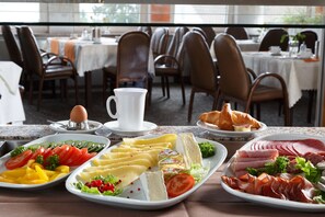 Un bufé de desayuno con una variedad de alimentos, incluyendo huevos, queso, carnes y pasteles.