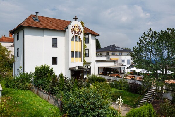 A white building with a red roof, a sign for a restaurant cafe, and a staircase leading to a covered area with outdoor seating.