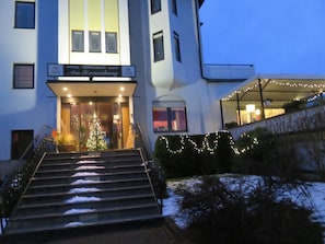 L’entrée d’un hôtel, avec un escalier, un sapin de Noël et une enseigne indiquant : « Hôtel Restaurant Café Am Pannenhang ».