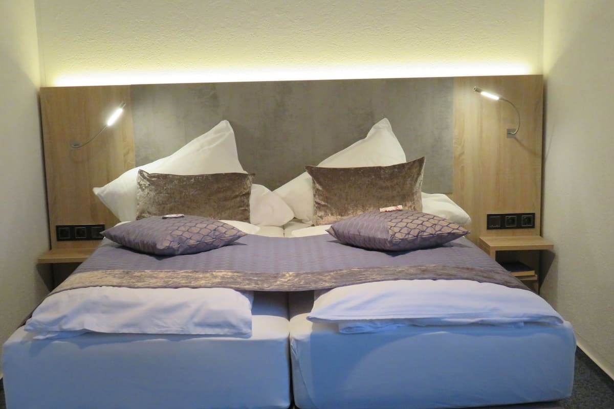 Un lit double avec une tête de lit en bois, deux tables de chevet et une petite table de nuit avec une lampe.
