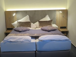 Un lit double avec une tête de lit en bois, deux tables de chevet et une petite table de nuit avec une lampe.