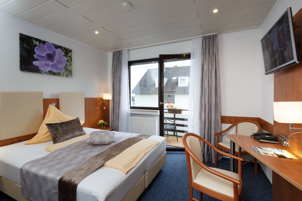 Une chambre d’hôtel comprenant un lit, un bureau, une chaise, une télévision et un balcon avec vue sur les maisons.
