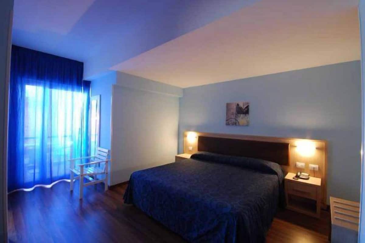 Ein Hotelzimmer mit einem Bett, Nachttischen, einem Sessel und einem Fenster mit Vorhängen.