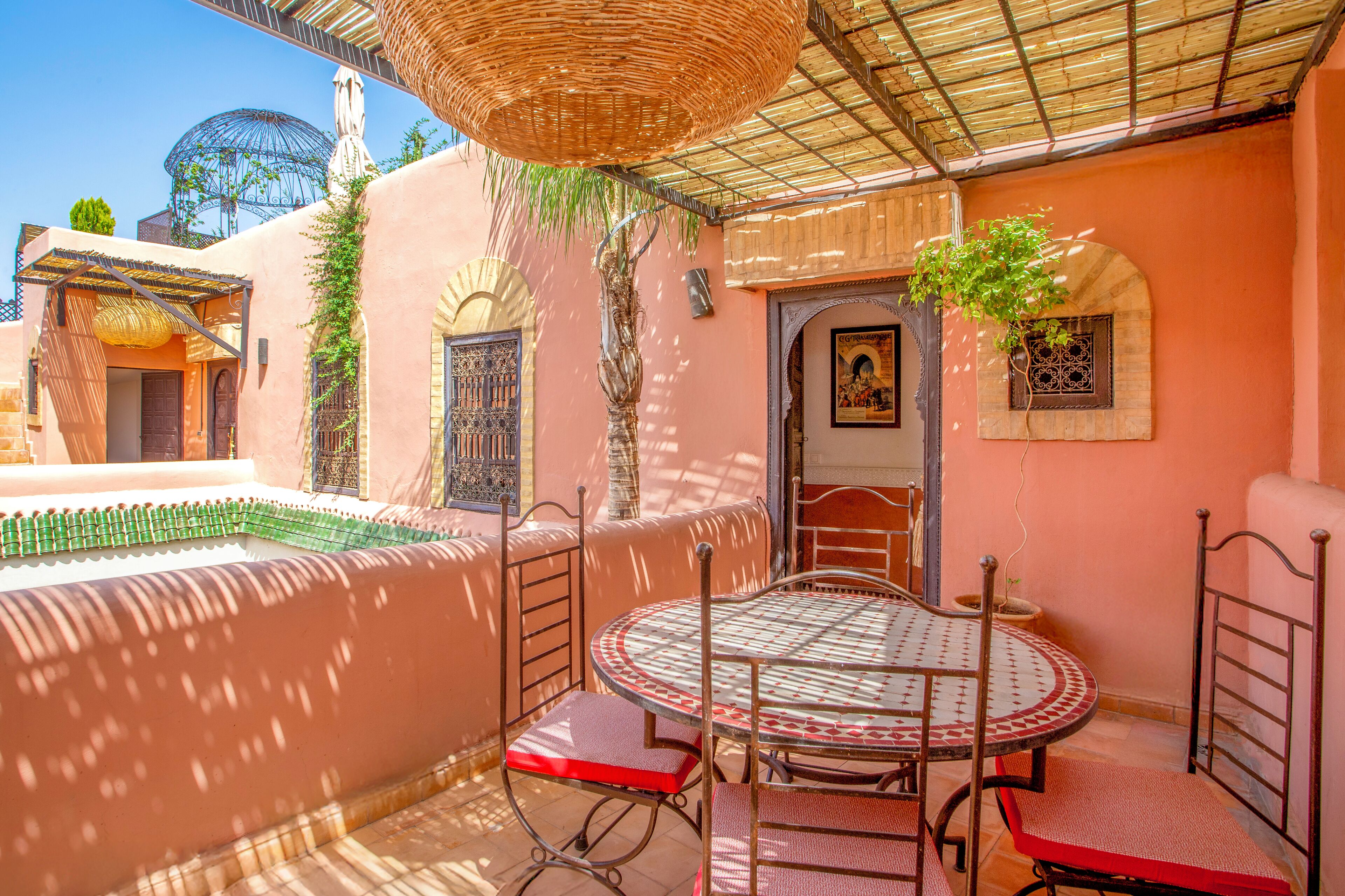 Un patio exterior acogedor con una mesa redonda y sillas, una cesta colgante y una puerta decorativa.