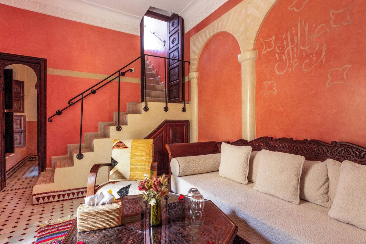 Una sala de estar con una escalera, un sofá, una mesa de centro con un jarrón y una alfombra estampada.