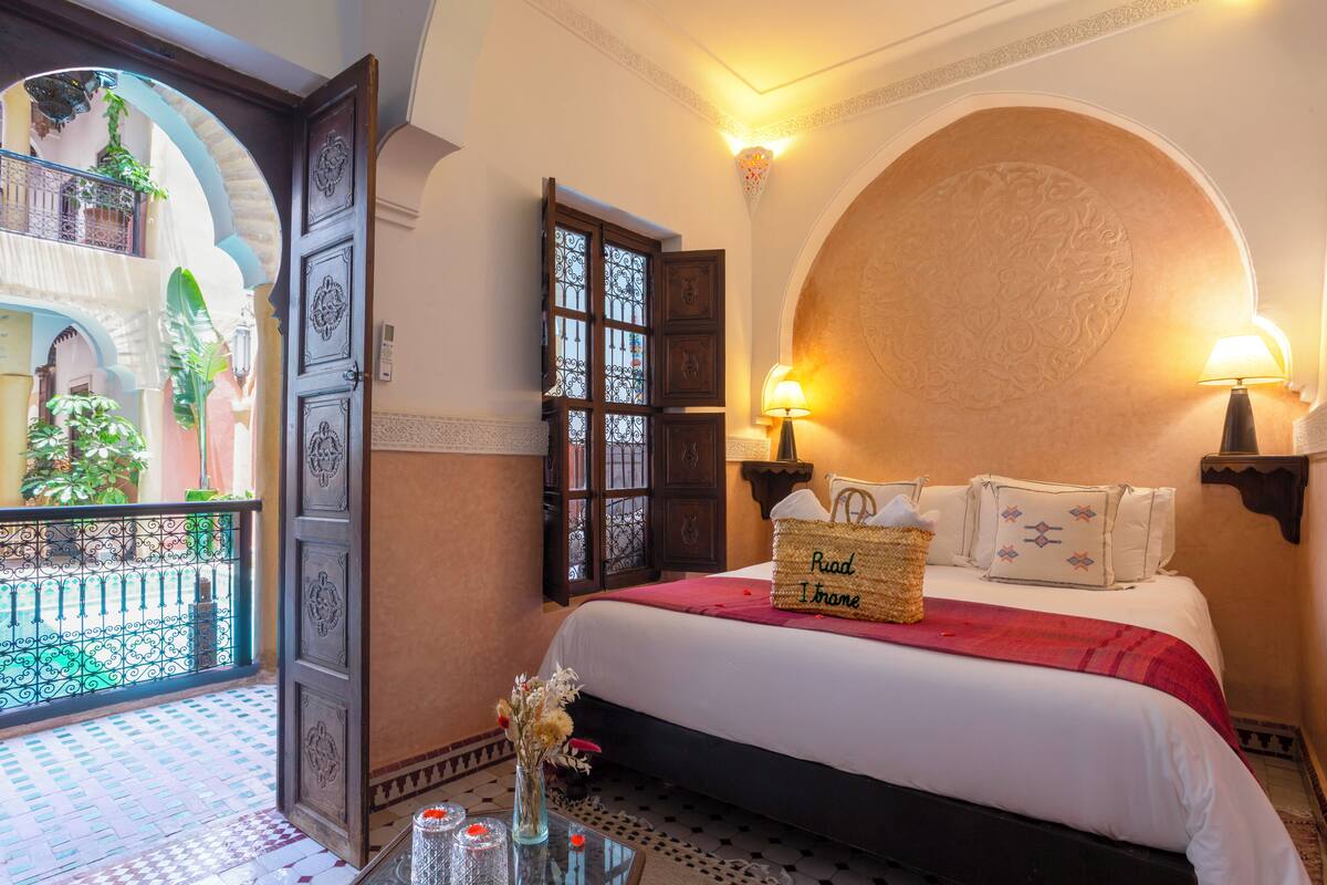 Una habitación de hotel con una cama, un balcón con plantas, una pared decorativa y una lámpara.