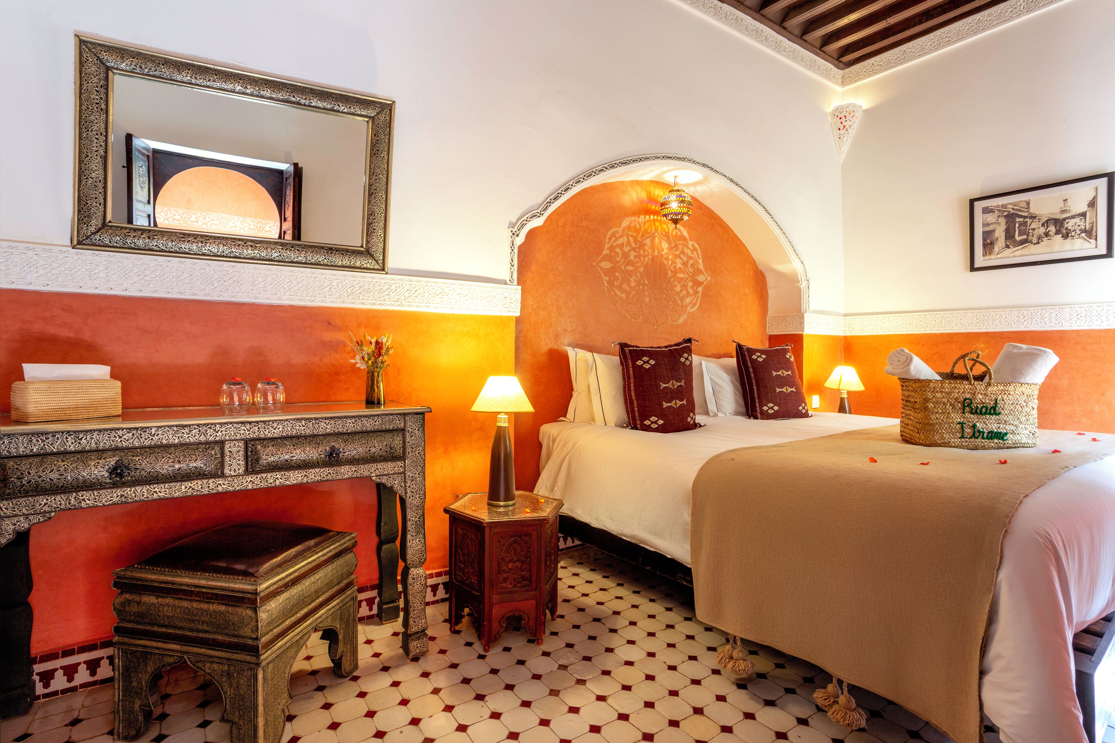 A hotel room with a bed, a nightstand, a lamp, a mirror, and a decorative wall arch.