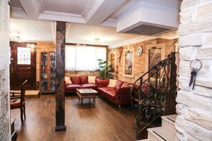 Un salón acogedor con un sofá rojo, suelo de madera y una escalera con barandilla decorativa.