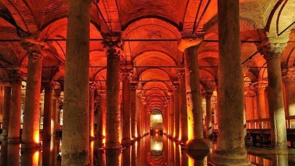 Un largo pasillo con techos altos y columnas que conduce a un área central con una fuente de luz.