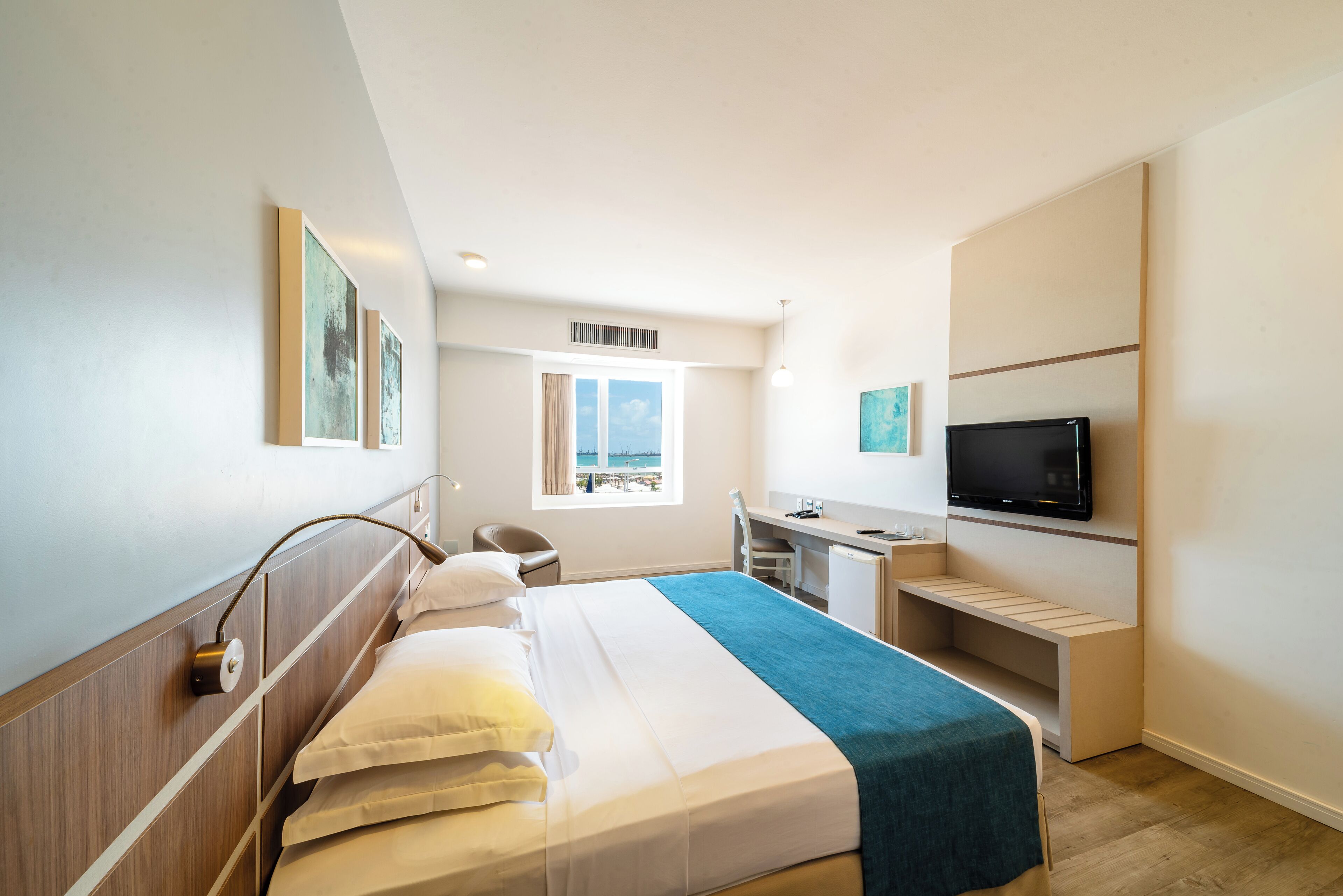 Habitación de hotel con cama, escritorio, silla, televisor y ventana con vistas.