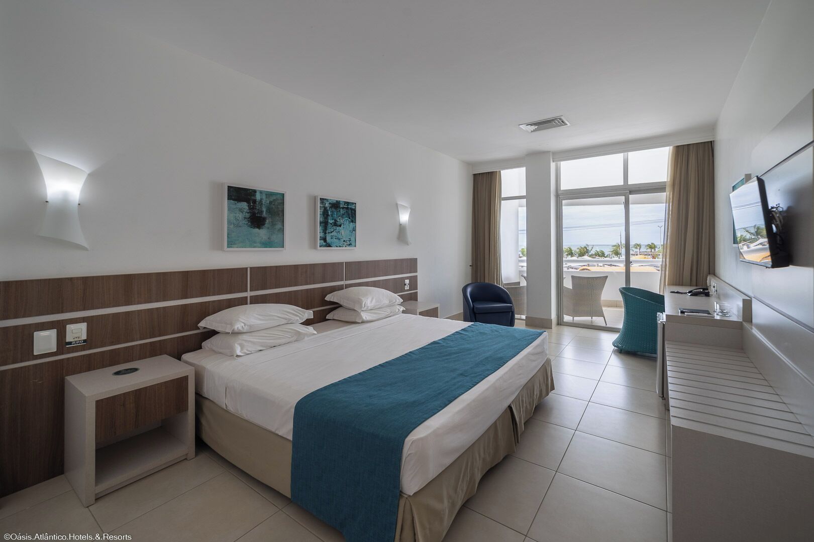A hotel room with a large bed, a desk, a chair, and a TV.