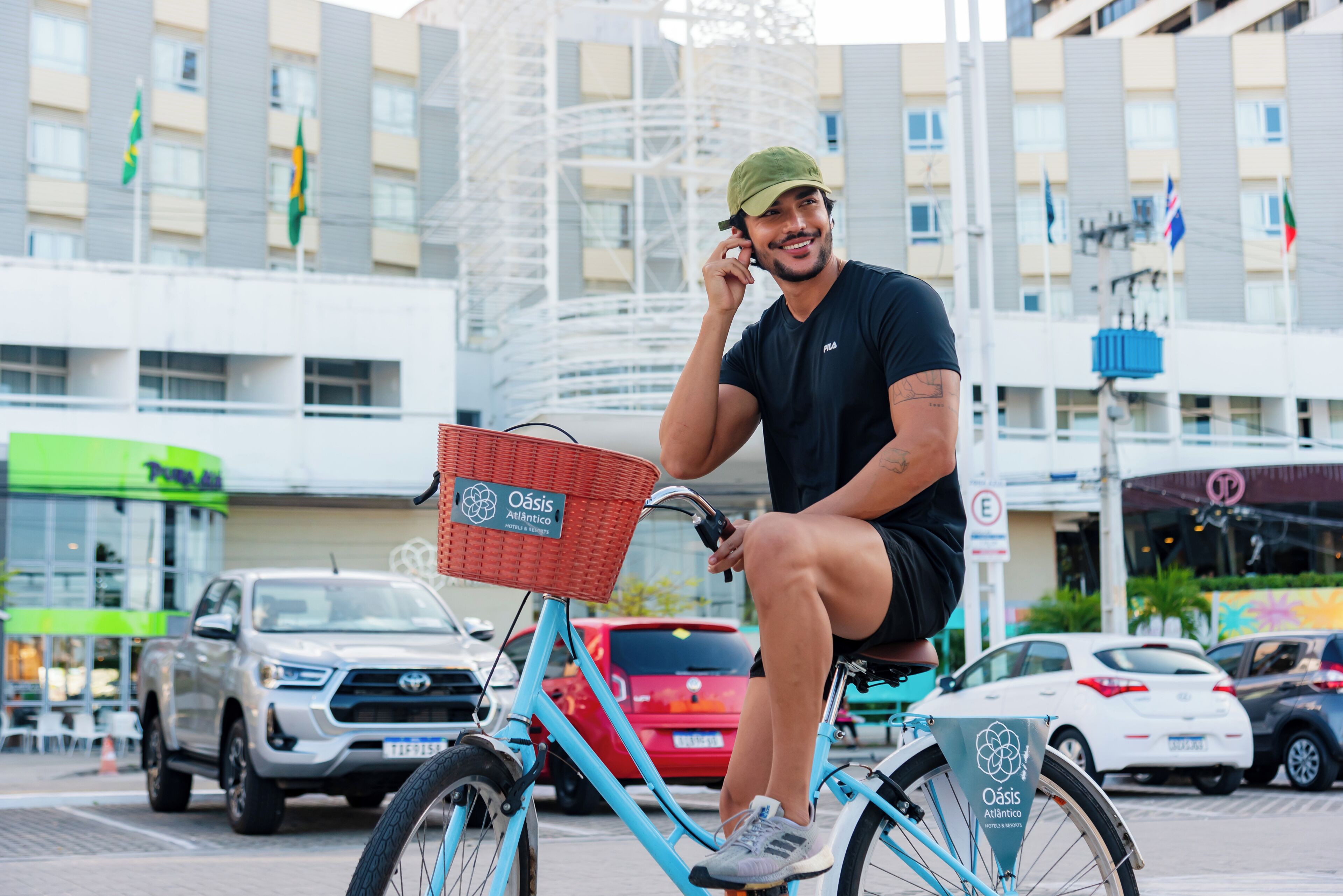 A person on a blue bicycle with a basket, in an urban setting with buildings and parked cars.