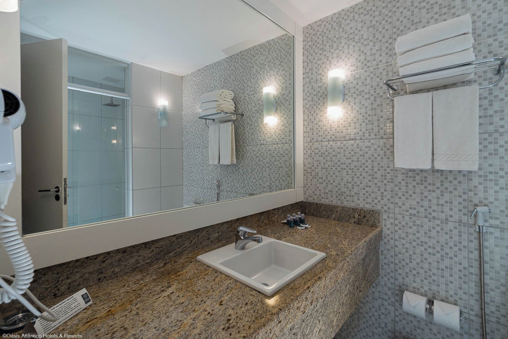 A modern bathroom with a granite countertop sink, a glass shower enclosure, and tiled walls.