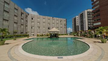 A modern hotel courtyard with a central swimming pool, surrounded by greenery and adjacent to multi-story buildings.