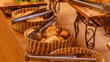 Uma mesa de buffet com diversos pães, pãezinhos e doces.