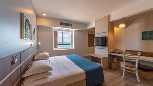 Habitación de hotel con cama, escritorio, silla, televisión y ventana con vistas.