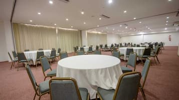 Uma sala de conferência com mesas e cadeiras redondas, piso coberto de carpete e cortinas nas janelas.