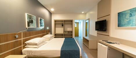 Habitación de hotel con cama, mesita de noche, armario, televisor y kitchenette.