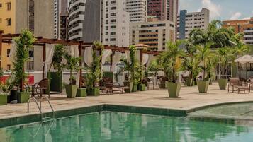 Una piscina al aire libre, sombrillas, sillones reclinables de piscina