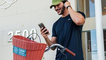 Una persona de pie junto a una bicicleta azul claro con una cesta roja, frente a un edificio con un letrero que dice 'oasis Atlanticico' y el número '2500'.