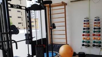 Un gimnasio con máquina Smith, pesas libres, banca, trampolín y un soporte de mancuernas en la pared.
