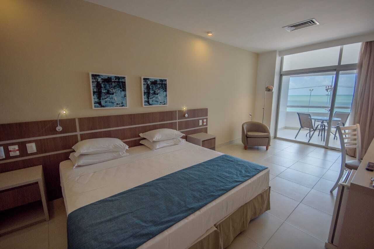 Habitación de hotel con una cama grande, un escritorio y una silla. Hay una ventana con vista al océano.