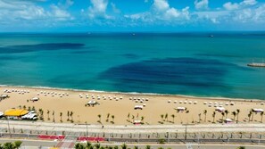 A beach with rows of umbrellas and beach chairs, a road in the foreground, and the ocean in the background.