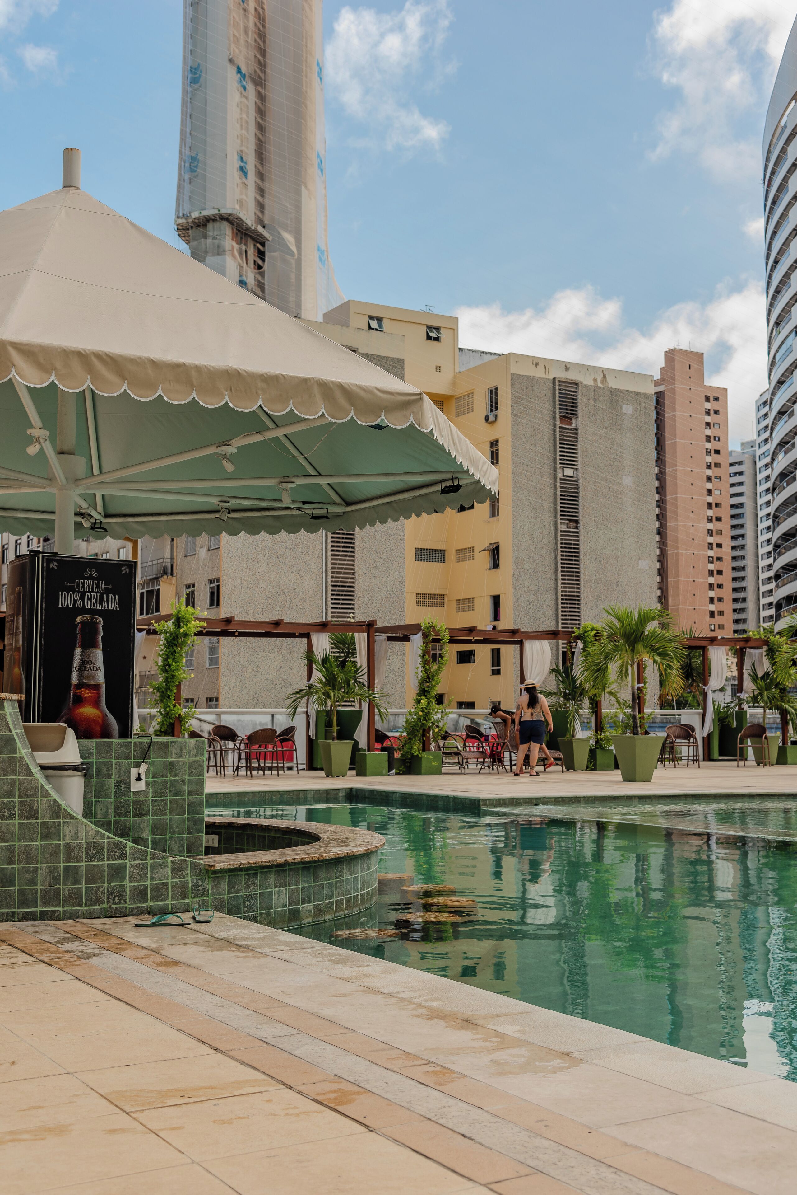 A rooftop pool area with a pergola, lounge chairs, and a large beer advertisement.