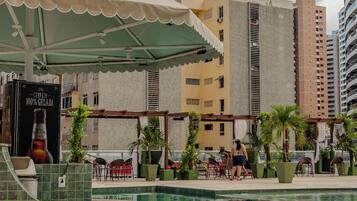 A rooftop pool area with a pergola, lounge chairs, and a large beer advertisement.