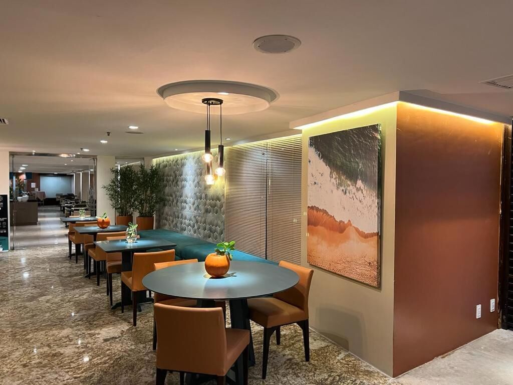 Uma sala de jantar moderna com mesas redondas e cadeiras laranja, um grande lustre fixado na parede e um quadro grande na parede.