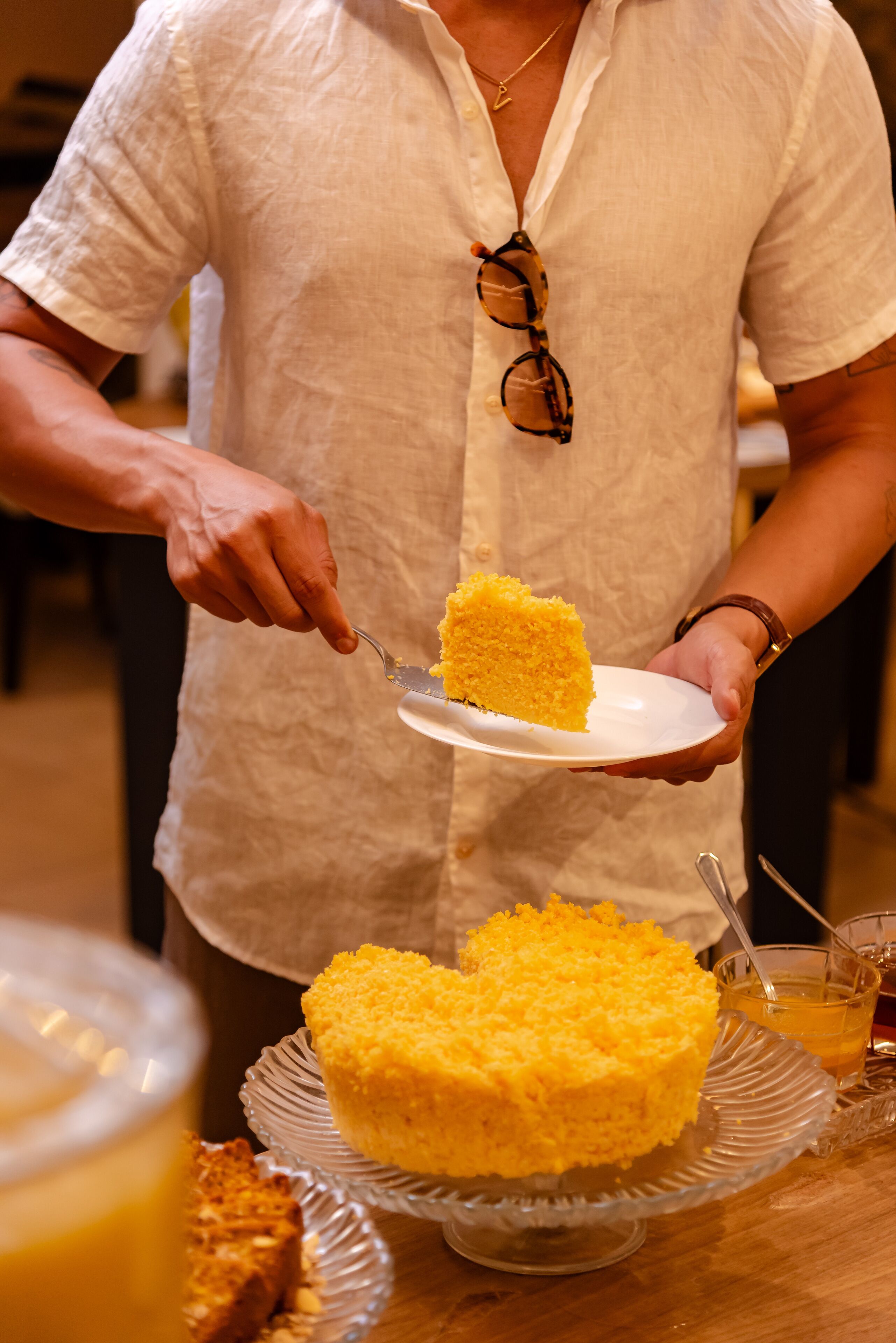 A person serving a slice of yellow cake on a white plate.