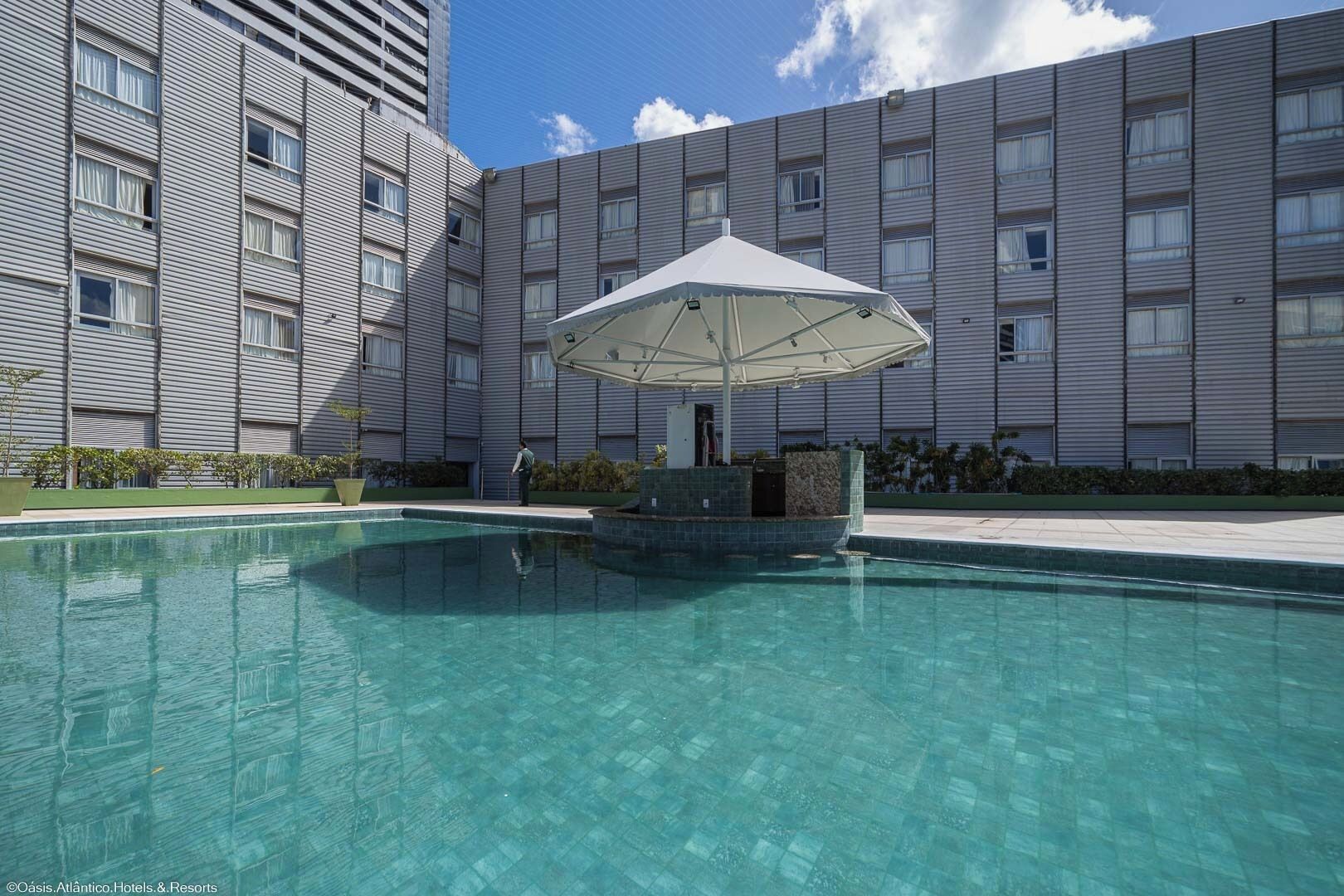 Une piscine dotée d’un espace de repos couvert, entourée d’un bâtiment moderne avec de nombreuses fenêtres.