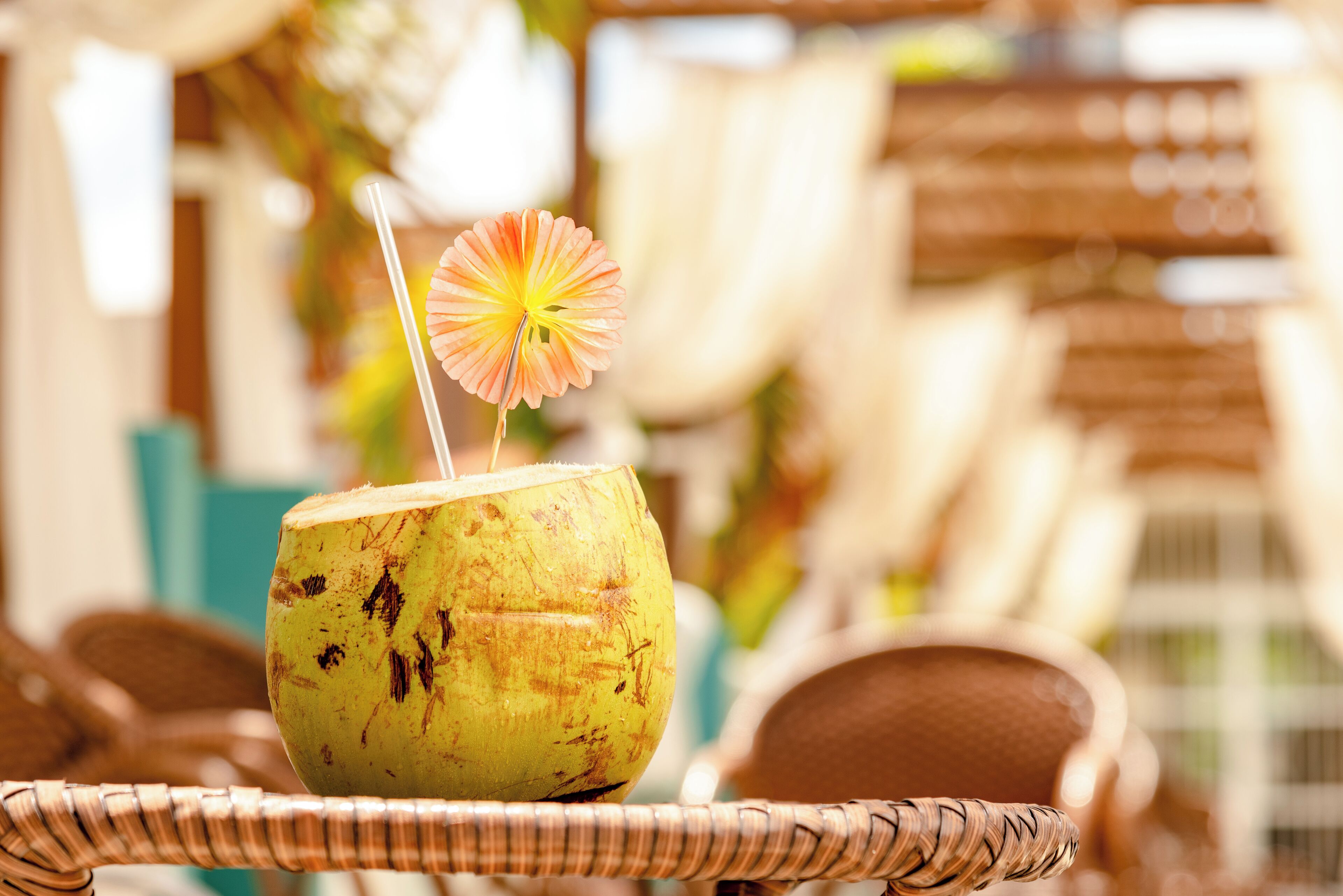 A yellow coconut with a straw and a flower on top, placed on a wicker chair.