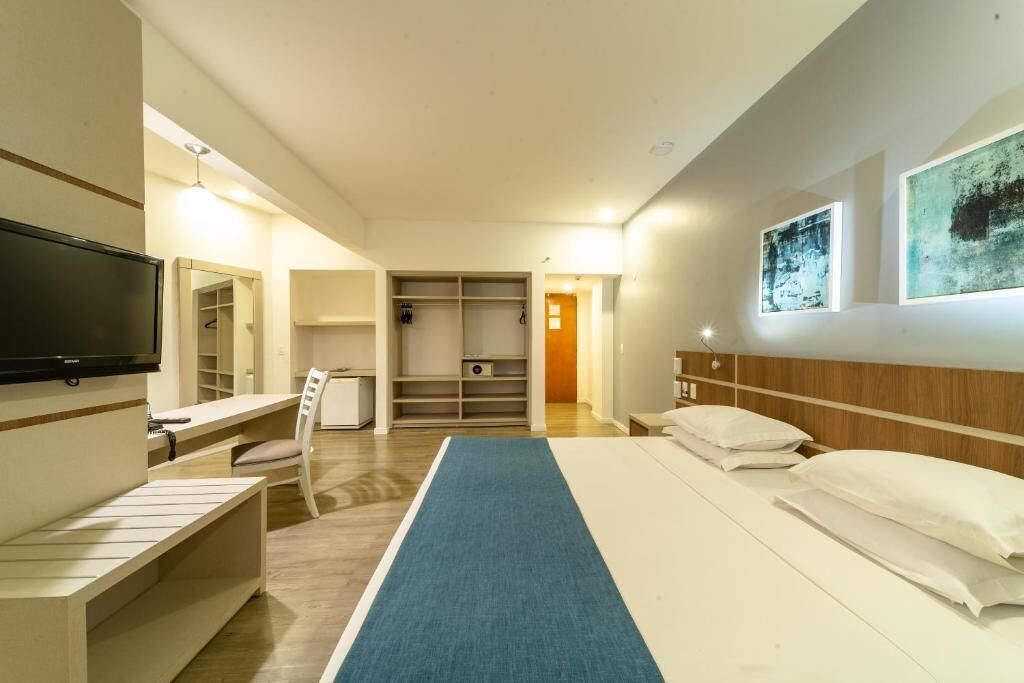 Ein Hotelzimmer mit einem Bett, einem Fernseher, einem Schreibtisch, einem Sessel, einem Kleiderschrank und Bildern an der Wand.