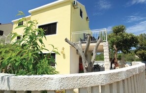 A yellow building with a balcony, surrounded by greenery and a stone wall. - Dragan´s Den Hostel (Korcula)