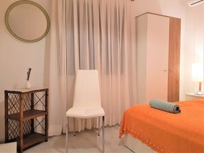 A bedroom with a bed, a chair, a small table with a vase, and a wardrobe. - Dragan´s Den Hostel (Korcula)