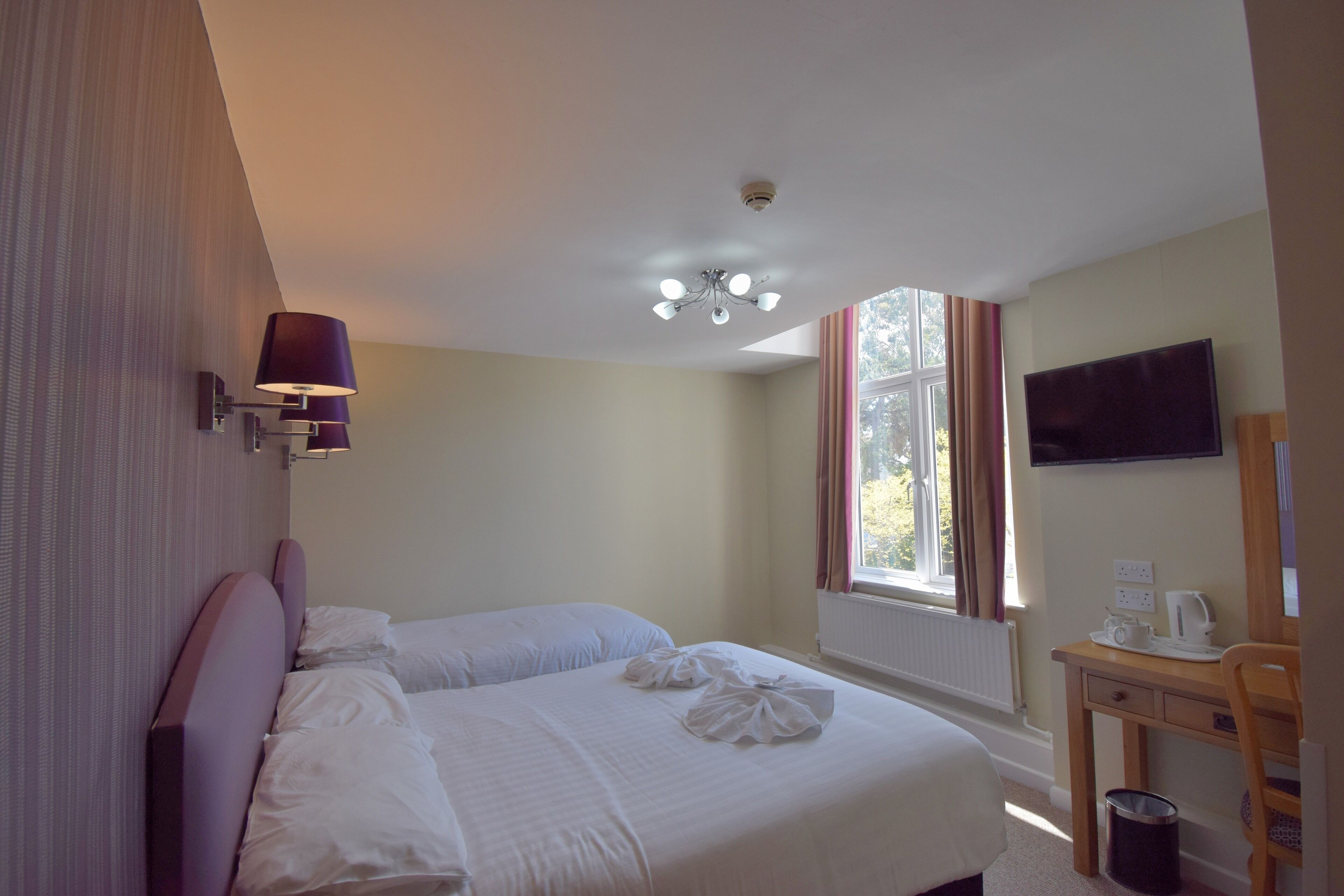 A hotel room with two beds, a desk with a chair, a TV, and a window with curtains.