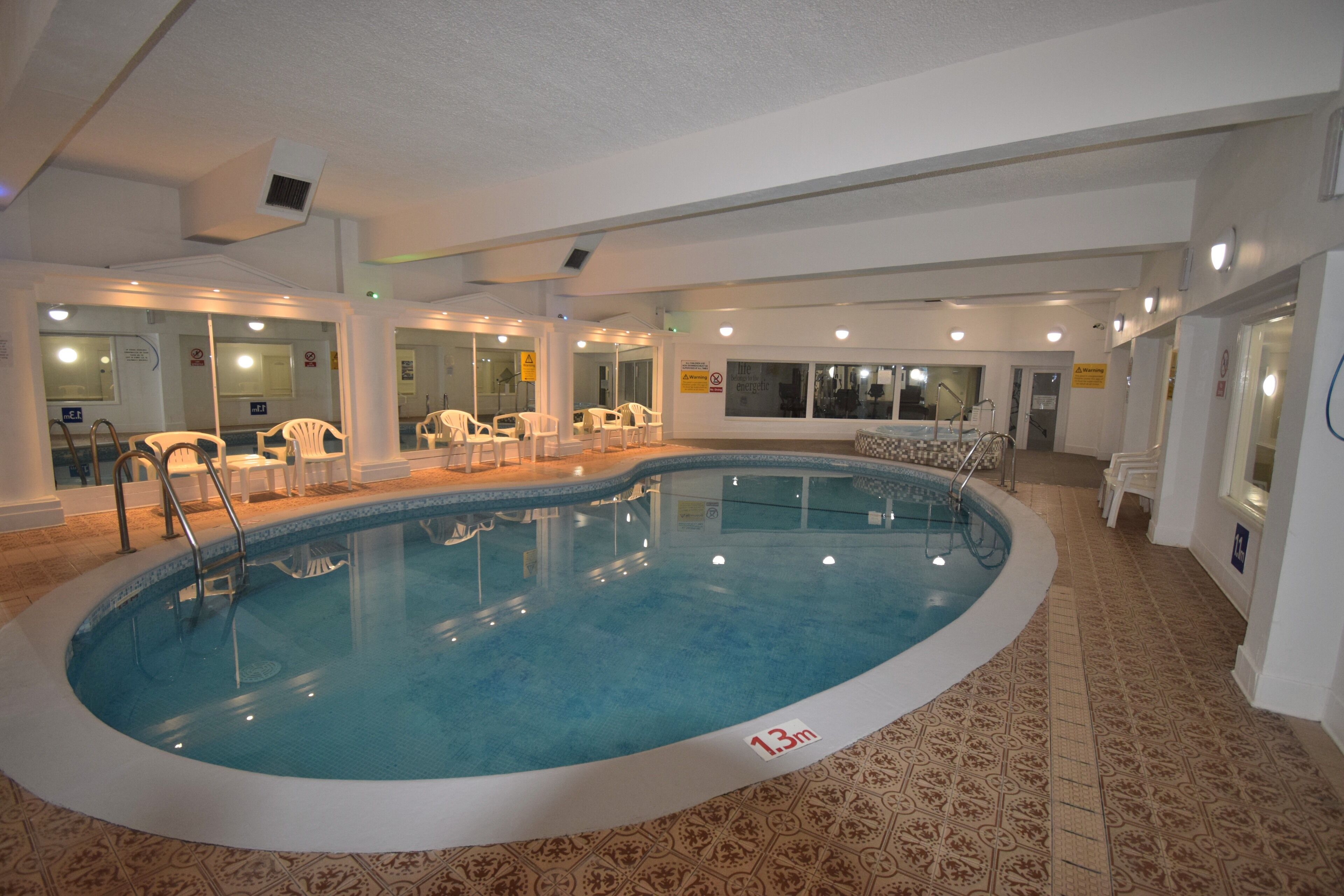 An indoor swimming pool with a 1.3m depth marker, surrounded by white chairs and a patterned floor.