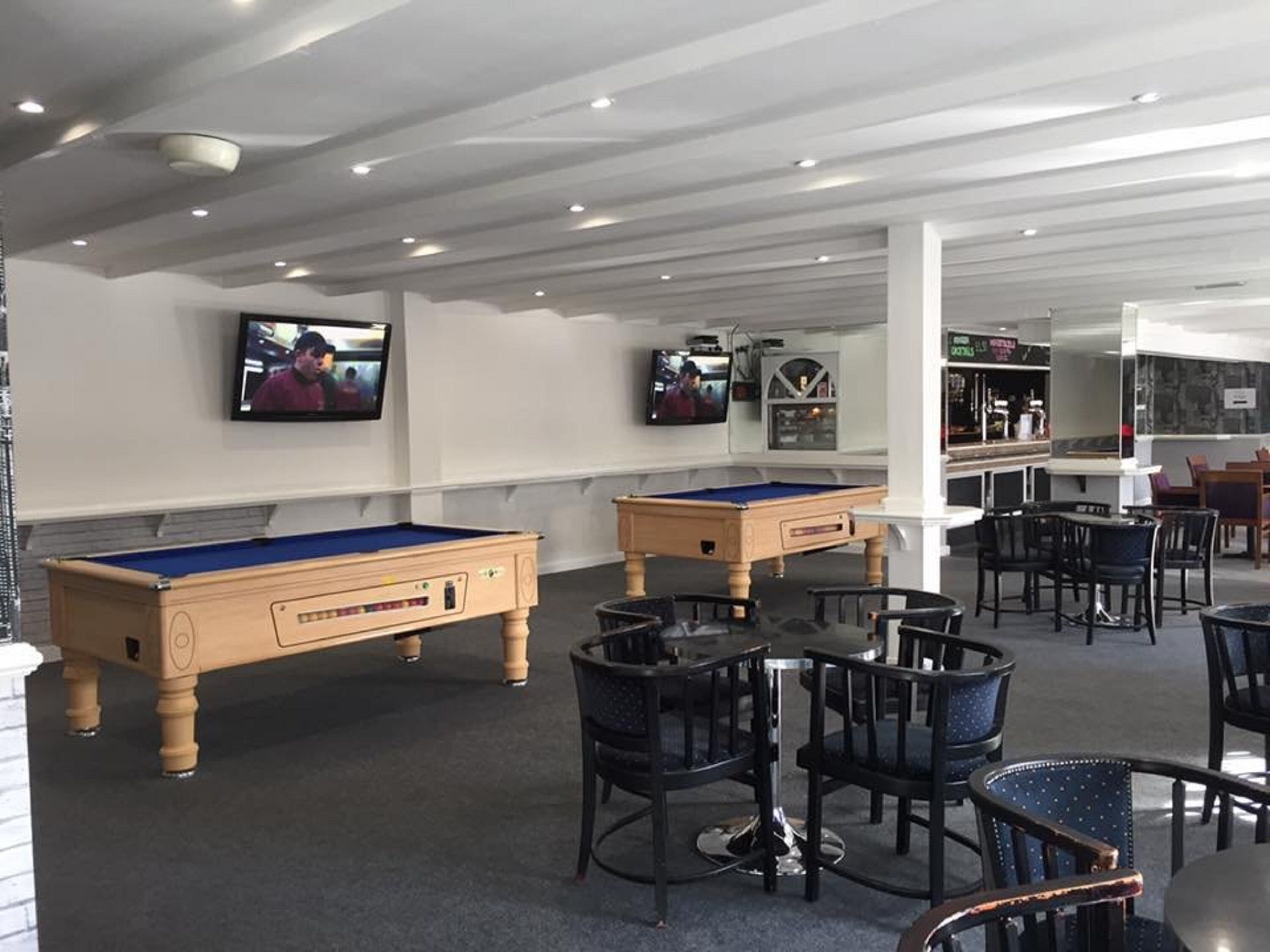 A pool table area with two pool tables, a bar, and seating.