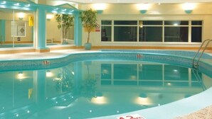 An indoor swimming pool with clear depth markers, a tiled floor, and a surrounding area with benches and a potted plant. - Riviera Hotel (Torquay)