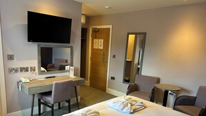 A hotel room with a bed, a desk, a chair, a TV, a mirror, and a door. - Riviera Hotel (Torquay)