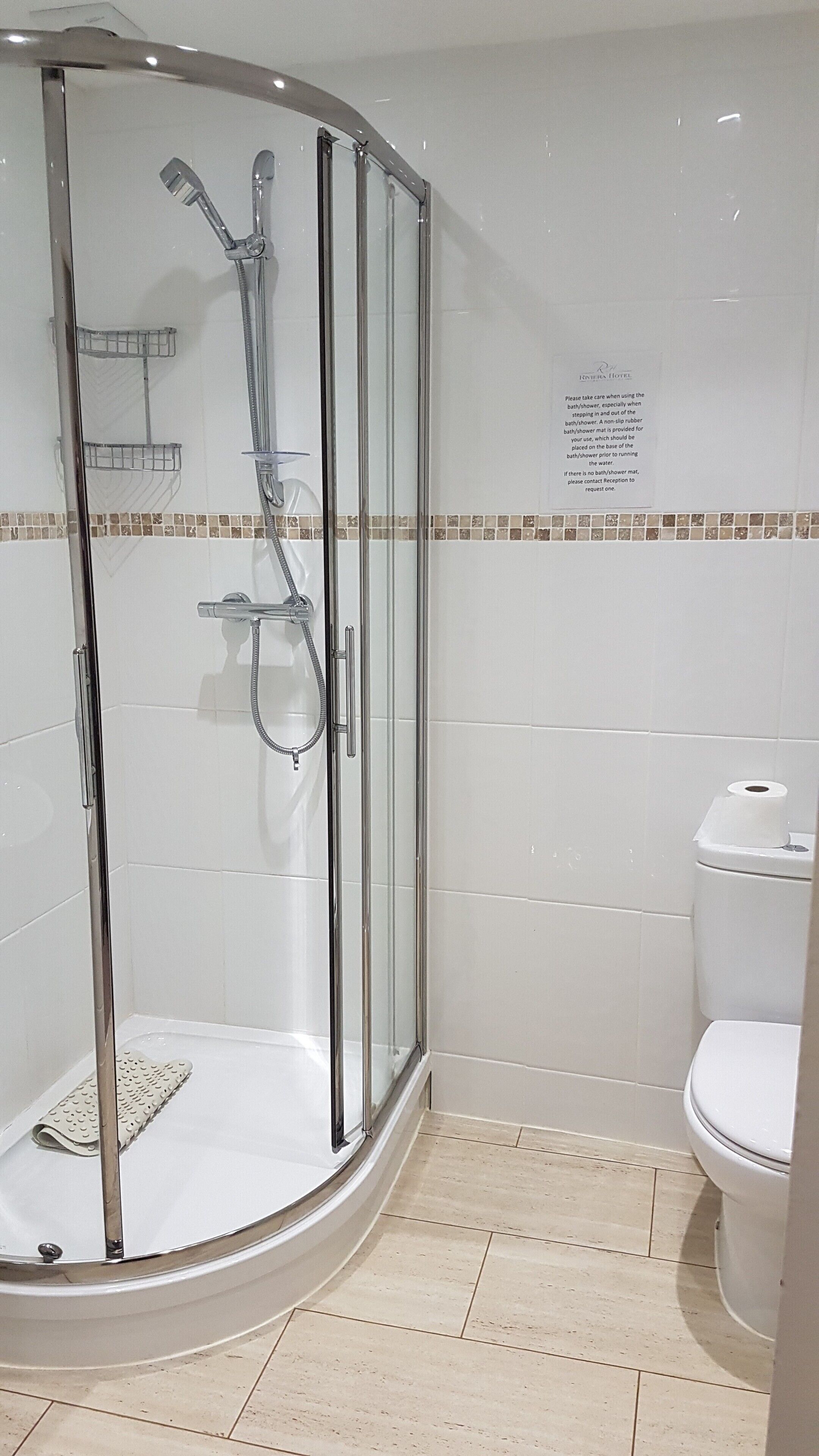 Área de chuveiro com paredes de vidro, incluindo vaso sanitário e dispensador de papel.