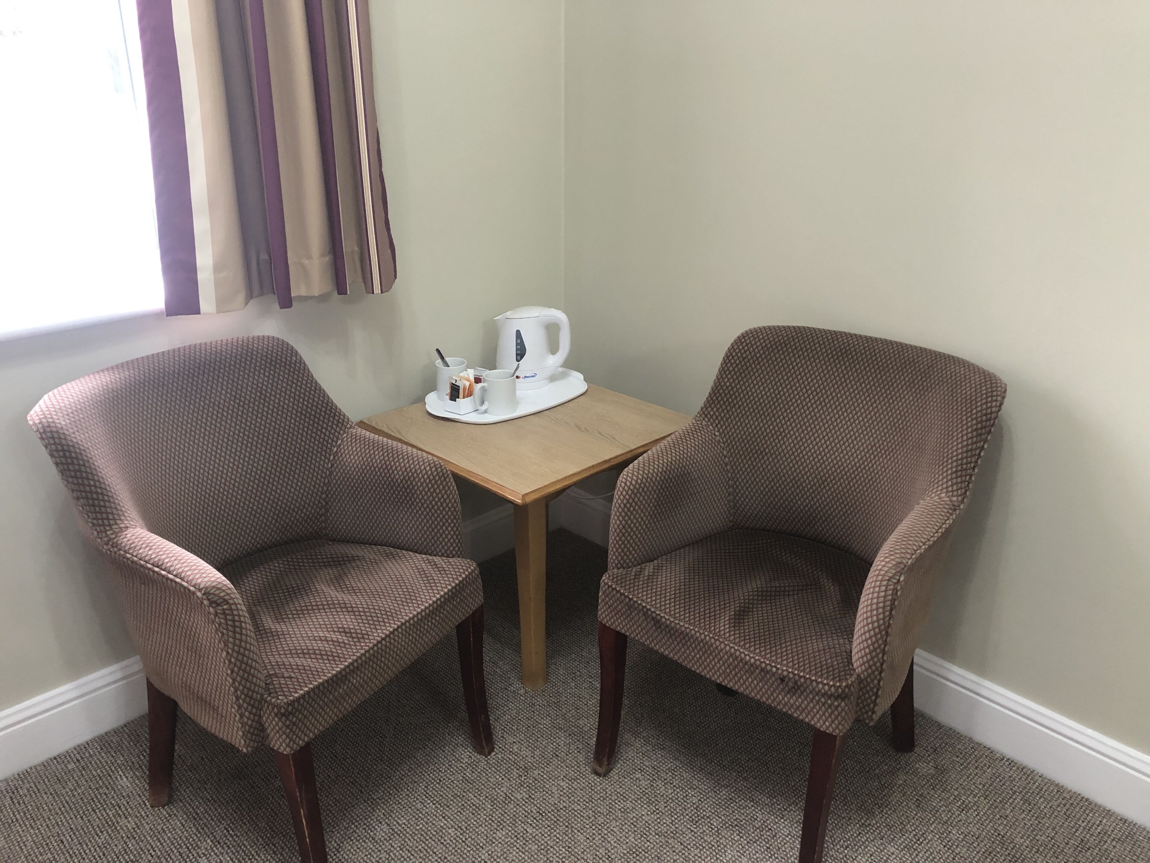 A room with two brown patterned chairs, a small wooden table, and a white kettle.