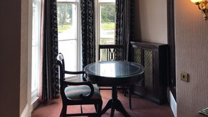 A dining area with a round table and chairs, large windows with curtains, a chandelier, and a wall-mounted light fixture. - Riviera Hotel (Torquay)