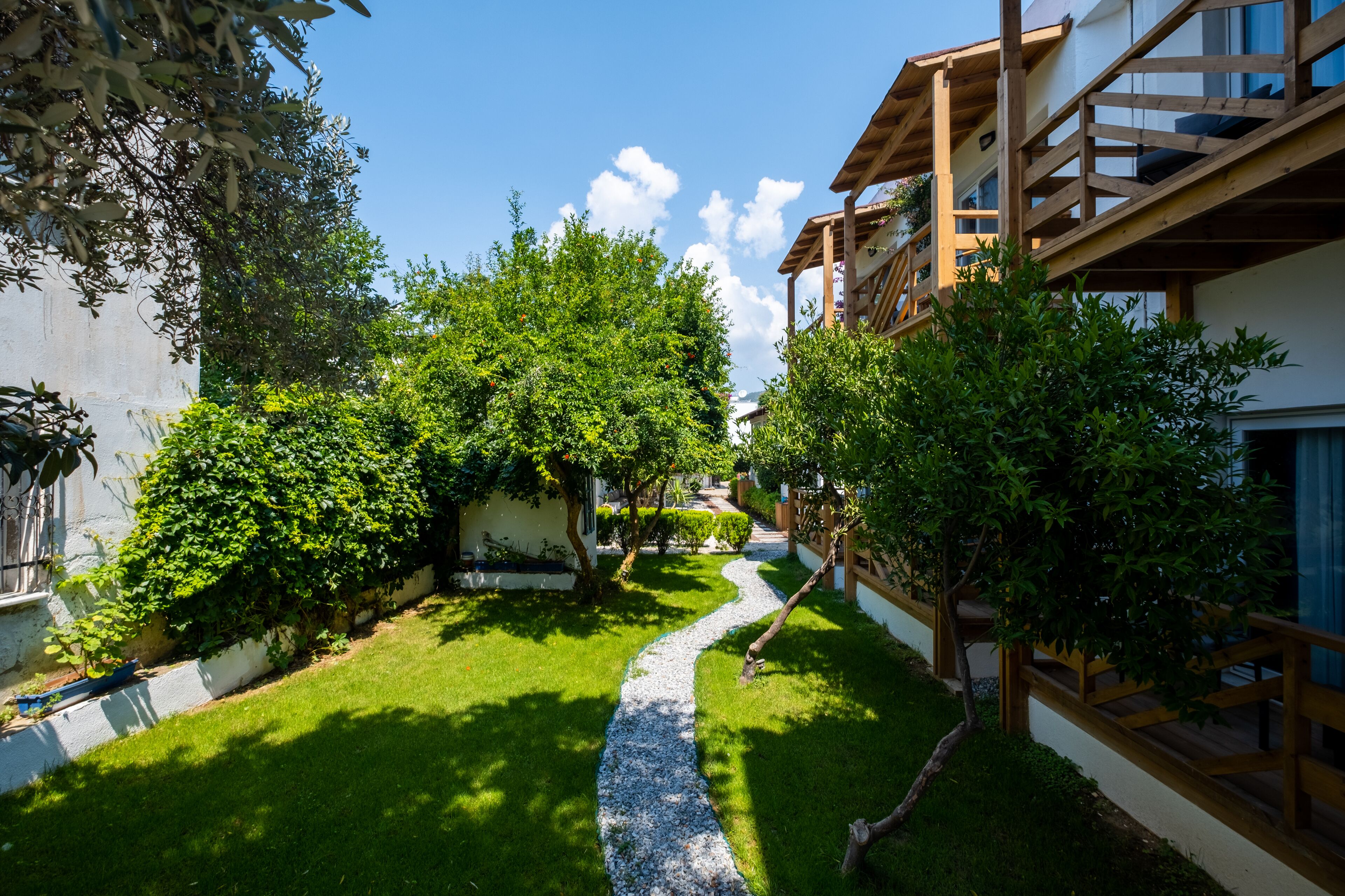 Une cour avec un chemin de gravier, une végétation luxuriante et une structure de balcon en bois.