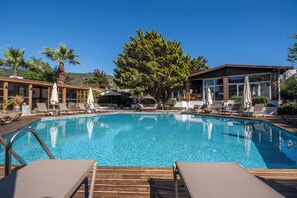 Una piscina al aire libre, sombrillas, sillones reclinables de piscina
