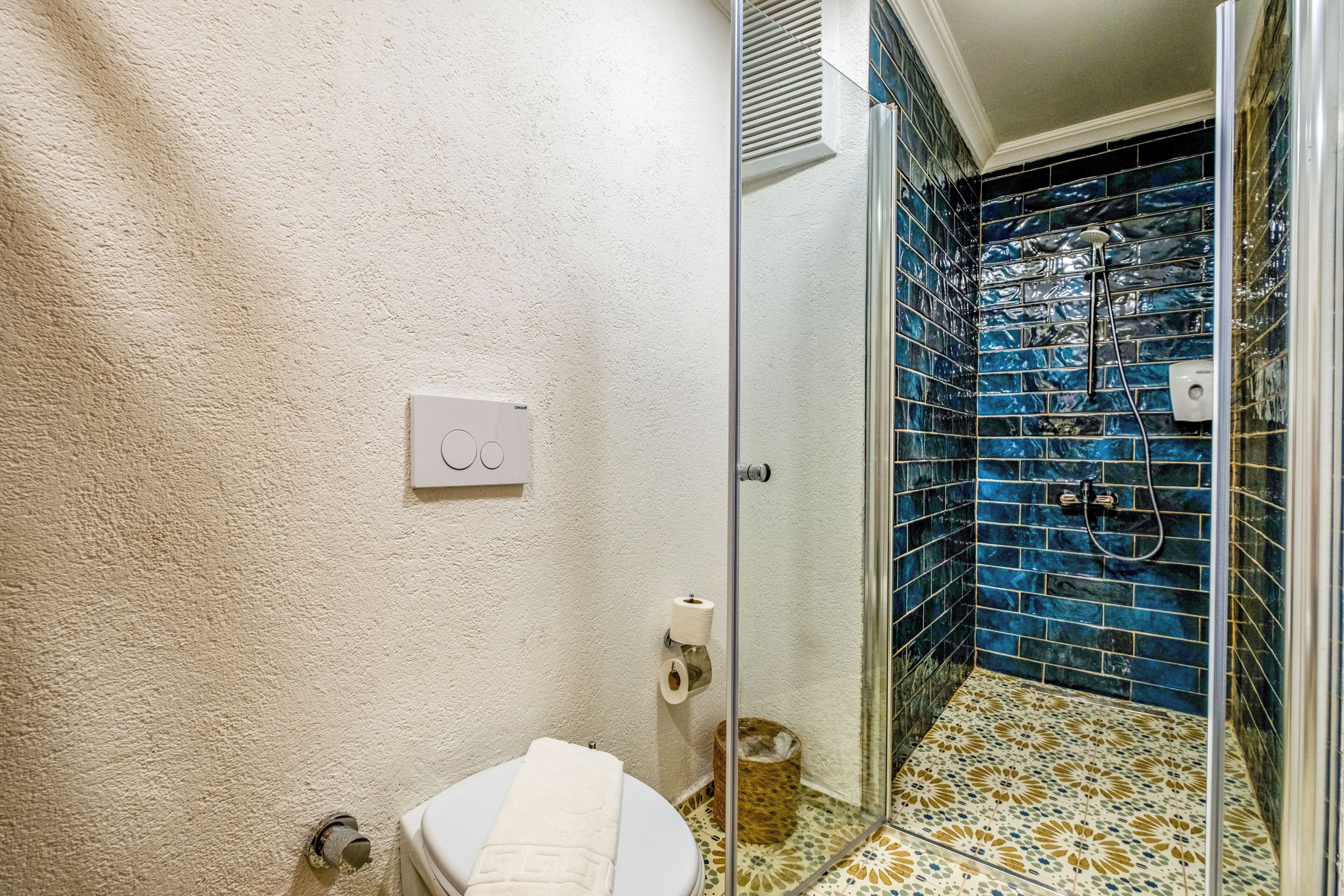 A bathroom with a toilet, a glass shower enclosure, and a wall-mounted toilet paper holder.